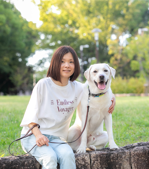 芝生に座って愛犬とカメラを見る代表 片岡果純