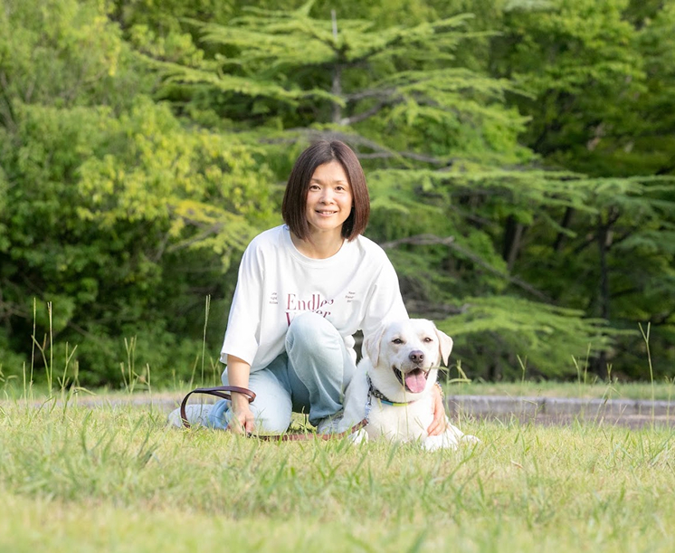 木立の前で愛犬と笑顔を見せる代表
